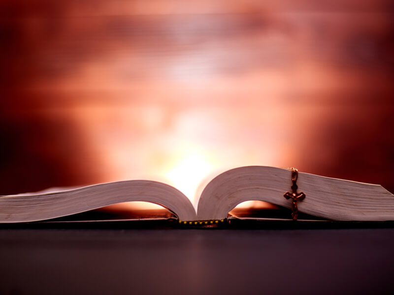 An Open Bible And A Church Cross In Dark Colors And A Shining Ba